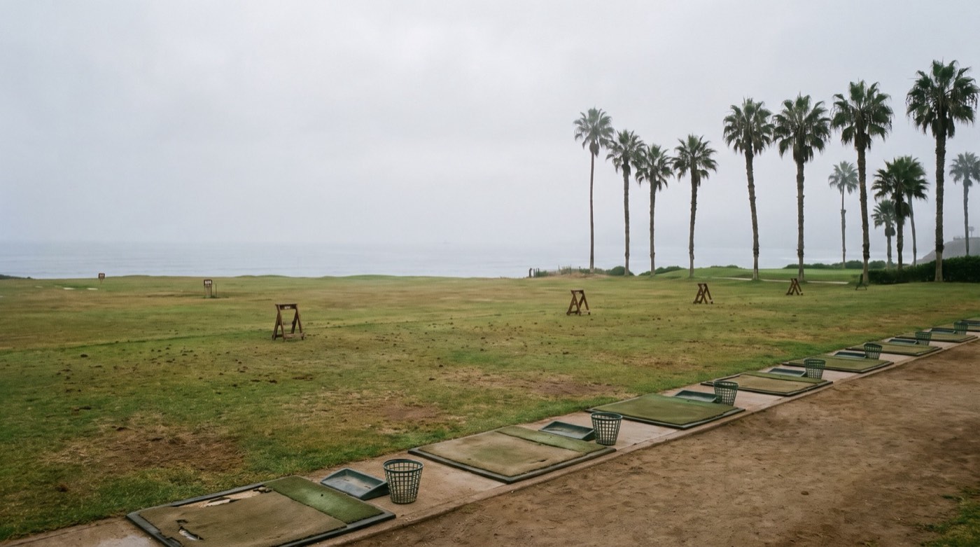 La línea de esteras de la cancha de práctica frente a un campo abierto que termina en el mar, con palmeras entre la neblina